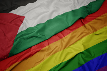waving colorful gay rainbow flag and national flag of palestine.