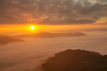Mountain view morning of top hill around with sea of mist in valley with orange sun light and cloudy sky background, sunrise at Pha Tang, Chiang Rai, northern of Thailand.