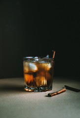 Whiskey with ice cubes and cinnamon stick on dark background. Autumn alcohol concept