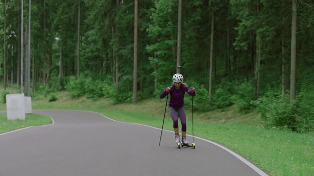 TRACKING Caucasian female professional biathlete roller skiing uphill on a forest track during mid-season practice in summer. ARRI Alexa Mini with Cooke S4 prime lenses RAW graded footage