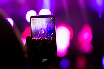 At a music festival, he creates live video on a fan smartphone and shares it on a social networking site. There are no recognizable faces, only hands and stage lights. - 282441694