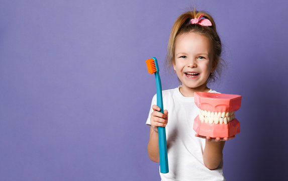 Laughing Kid Girl Shows Us Big Dental Implant Model And Giant Toothbrush On Purple With Free Text Copy Space