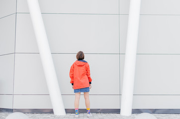 A short haired woman in coral windbreaker and colorful socks staying back on road near grey wall © Bohdan Melnyk