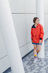 A short haired woman in coral windbreaker and colorful socks staying on road near grey wall © Bohdan Melnyk