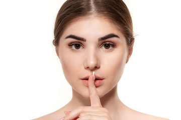 Close-up portrait of a beautiful young girl holding finger near her mouth expressing idea of secret isolated over white background.