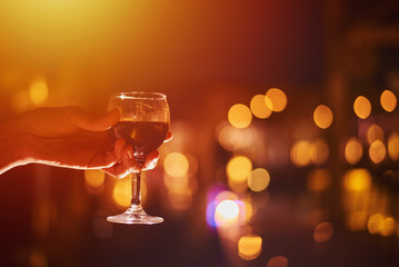 wineglass with wine in a woman hand against defocused lights, close up