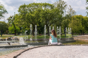 People, travel and summer holidays concept. Young woman in the beautiful green garden enjoy the view of the fountain. Mestsky or City park of Kosice, Slovakia (Slovensko)