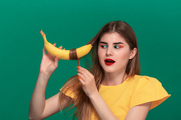 Fototapeta premium Portrait of beautiful young woman with bright color make-up jokingly curling hair with banana.