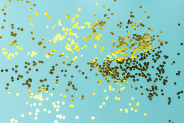 Turquoise festive background with golden confetti. The surface is strewn with shiny sparkles. Flat lay, top view.
