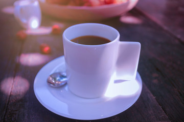 a white modern mug of black coffee serving on wooden table in morning sunlight