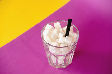 Glass full of sugar cubes  on purple background. Diabetes, sugar disease, unhealthy food, diet concept. Copy space
