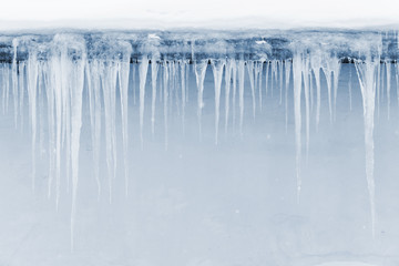 Icicles hang on the roof over light blue wall - obrazy, fototapety, plakaty