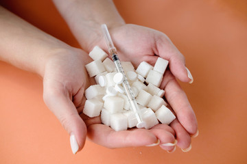 Woman holding white sugar cubes and  insulin syringe on orange background. Diabetes, sugar disease, unhealthy food, diet concept. Copy space