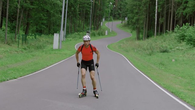 TRACKING Caucasian male professional biathlete roller skiing uphill on a forest track during mid-season practice in summer. ARRI Alexa Mini with Cooke S4 prime lenses RAW graded footage