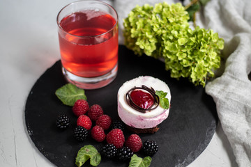 A glass with a compote of berries, next to a plate with blackberries, blueberries, raspberries. All this on a dark background, decorated with flowers.