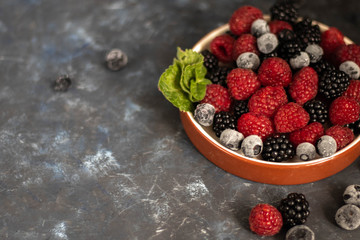 A glass with a compote of berries, next to a plate with blackberries, blueberries, raspberries. All this on a dark background, decorated with flowers.