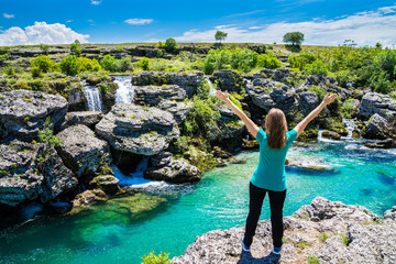 Montenegro, Pretty blonde young woman standing with arms stretched amazed at azure water of cijevna...