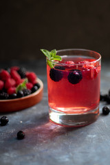 A glass with a compote of berries, next to a plate with blackberries, blueberries, raspberries. All this on a dark background, decorated with flowers.