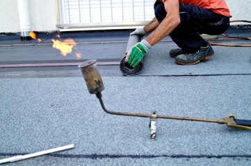 worker installing tar foil on the rooftop of building. Flat roof installation. Waterproof system by...