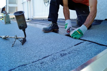 worker installing tar foil on the rooftop of building. Flat roof installation. Waterproof system by...