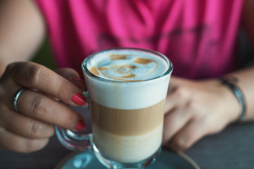 Female hands with latte coffee in cafe, close up