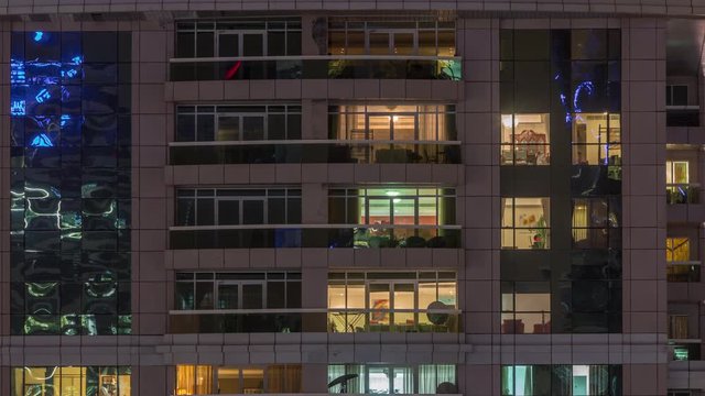 Night view of exterior apartment building timelapse. High rise skyscraper with blinking lights in windows with people moving inside. Pan up