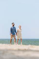 selective focus of adult couple walking along beach and holding hands