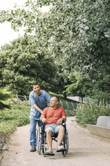 man in wheelchair walking with his caretaker