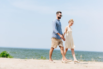 adult couple walking along sandy beach and holding hands