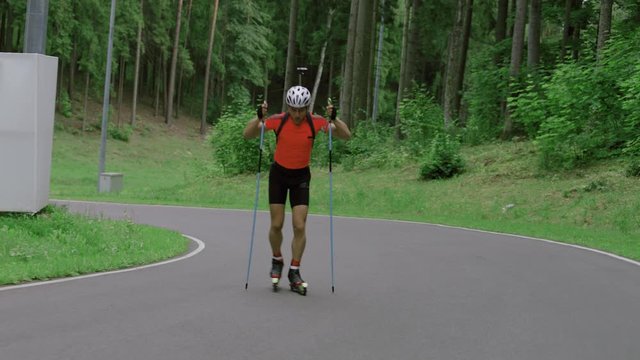 TRACKING Caucasian male professional biathlete roller skiing uphill on a forest track during mid-season practice in summer. ARRI Alexa Mini with Cooke S4 prime lenses RAW graded footage