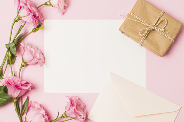 Blank paper with envelop; fresh pink flower and brown wrapped gift box over pink background