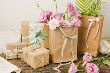 Paper bag full of fresh flowers and wrapped present gift over wooden surface