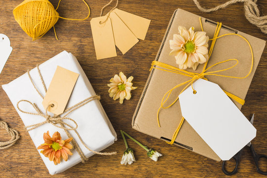 Wrapped gift tied with tag string and beautiful flower on wooden surface