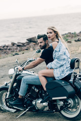 Fototapeta na wymiar young couple of bikers sitting on black motorcycle at beach near river