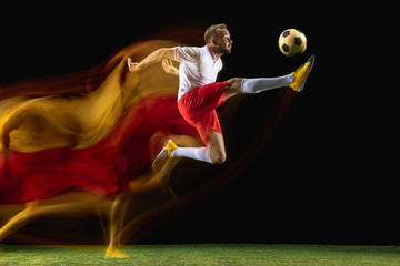 Jump. Young caucasian male football or soccer player in sportwear and boots kicking ball for the goal in mixed light on dark background. Concept of healthy lifestyle, professional sport, hobby.