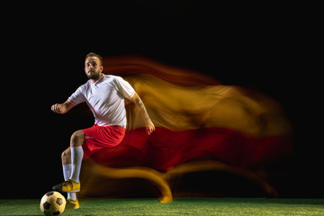 Emotions. Young caucasian male football or soccer player in sportwear and boots kicking ball for the goal in mixed light on dark background. Concept of healthy lifestyle, professional sport, hobby.