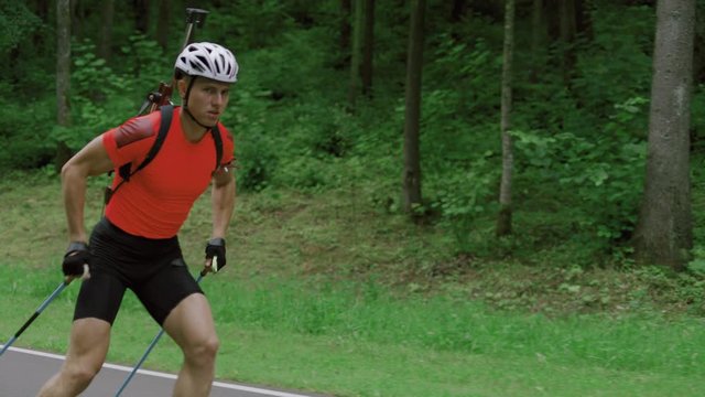 TRACKING Caucasian male professional biathlete roller skiing uphill on a forest track during mid-season practice in summer. ARRI Alexa Mini with Cooke S4 prime lenses RAW graded footage