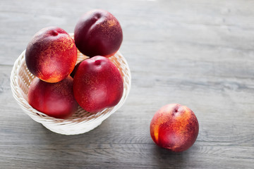 Ripe organic nectarines in white basket on  gray background.