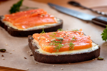 Sandwich of rye bread, salmon, butter, dill and seeds on a table close-up.