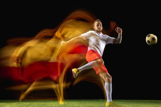 Chooses win. Young caucasian male football or soccer player in sportwear and boots kicking ball for the goal in mixed light on dark background. Concept of healthy lifestyle, professional sport, hobby. © master1305