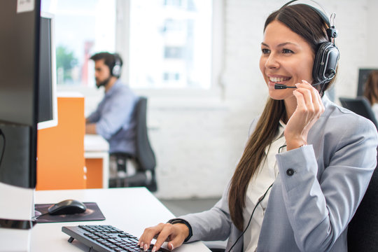 Beautiful young customer care operator with headset and microphone working in call centre