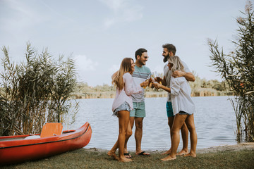 Fototapeta premium Group of friends with cider bottles standing by the boat near the beautiful lake and having fun