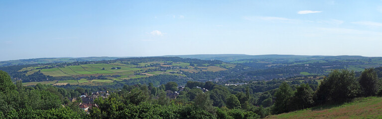 Obraz premium a long panoramic scenic view of west yorkshire countryside with the village of luddenden at the bottom of the calder valley with buildings surrounded by farms and fields