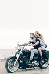 Fototapeta na wymiar happy young couple of bikers riding black motorcycle at sandy beach