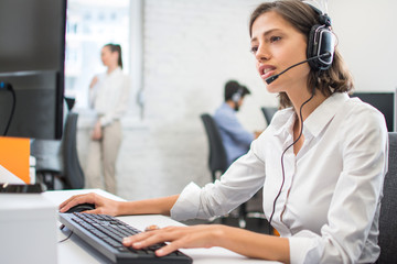 Beautiful friendly female customer support operator with headset using computer in call center