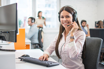 Positive female customer services agent with headset working in call center