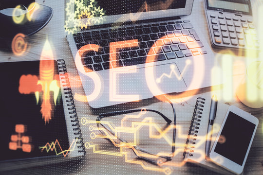 Double exposure of table with computer and seo drawing hologram. Search optimization concept.