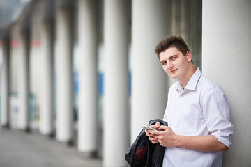 Young handsome businessman stands on the street near the business building and looks into the frame.