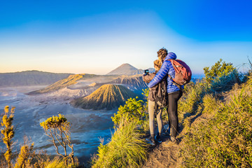 Obraz premium Young couple man and woman meet the sunrise at the Bromo Tengger Semeru National Park on the Java Island, Indonesia. They enjoy magnificent view on the Bromo or Gunung Bromo on Indonesian, Semeru and