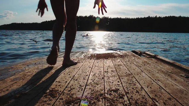 A teenager jumps from a dock into river water. Sunny summer day. Sunset time. Slow motion.